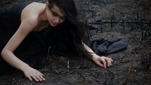 Woman Kneeling on Burned Ground in Black Dress