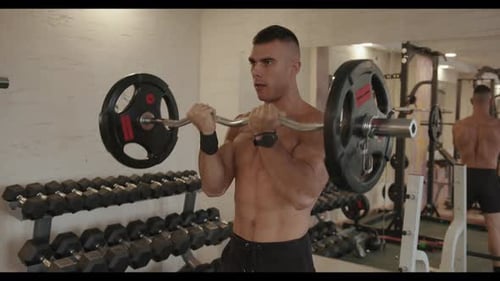 Young Bodybuilder in Black Sports Shorts Pumps Biceps with a z Barbells While Standing in Front of a