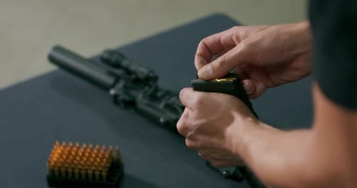 Nahaufnahme männlicher Hände, die Kugeln in einen Waffenmagazinclip auf einem Schießstand laden
