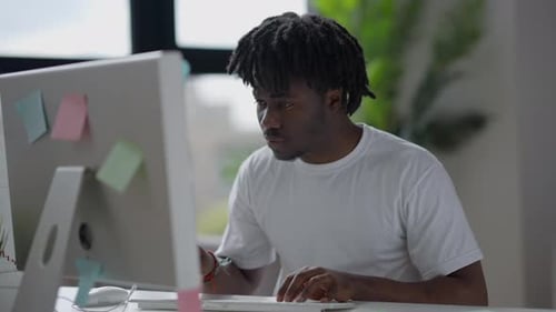 Porträt eines beschäftigten jungen Mannes, der auf der Tastatur tippt und auf den Bildschirm
