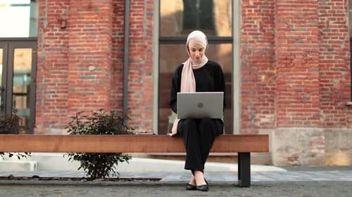 Cheerful Young Islamic Businesswoman Working on Laptop While Sitting Near Her Office