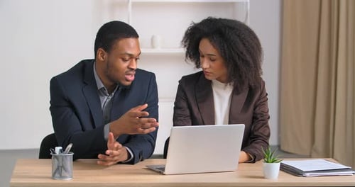 Two Colleagues Businesspersons Man and Woman Coworkers Sitting at Table in Modern Office Looking