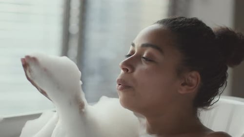 Junge schöne Afroamerikanerin badet zu Hause und bläst Schaum aus ihrer Handfläche und lächelt