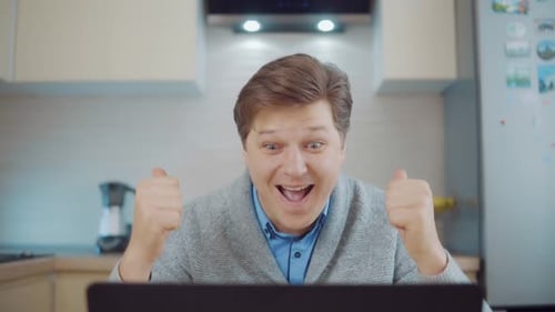 Man Celebrating Success at Laptop in Kitchen