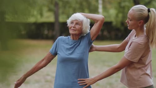 Senior Woman Exercising in Park with Help of Female Trainer