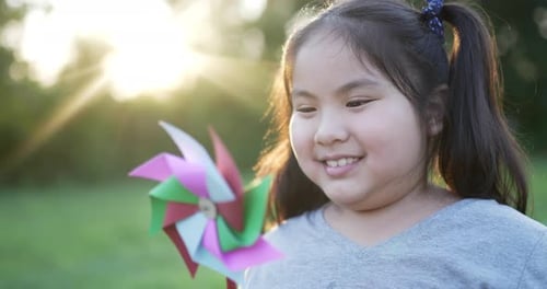 Funny asian girl with colored windmill in the garden