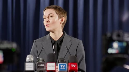 Woman Speaks at Press Conference, Cameras and Microphones
