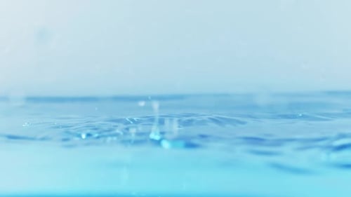 The clean water surface in slow motion fills the screen with water splashing shop the water drop and