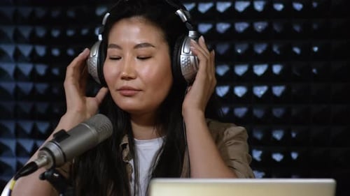 Woman with Headphones Speaking into Microphone in Studio