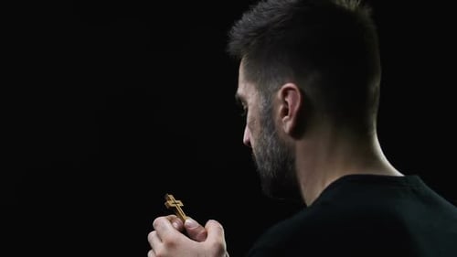 Man Holds Small Wooden Cross in Hand