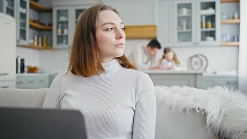 Close Up of Busy Woman Typing on Laptop at Home Looking Aside and Thinking Family on Background