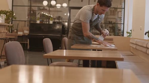 Man Cleaning Tables in Empty Cafe