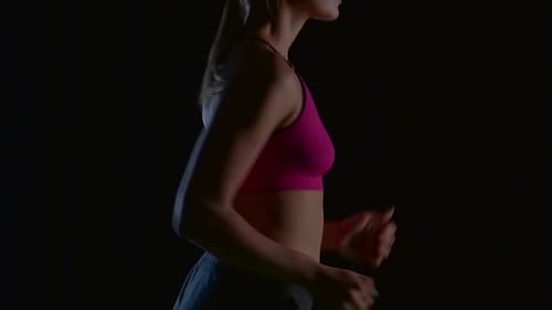 Sportlerin läuft auf schwarzem Hintergrund von der Seite. Zeitlupe. Nahaufnahme