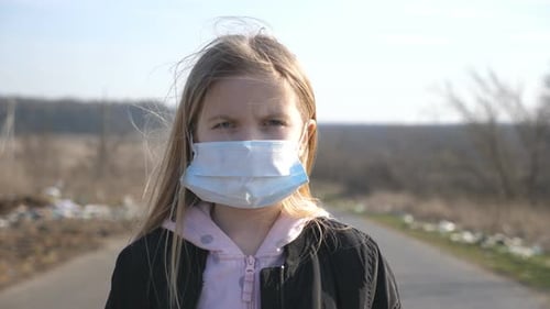 Portrait of Little Girl with Medical Face Mask Standing Outdoor. Sad Female Child Wearing Protective