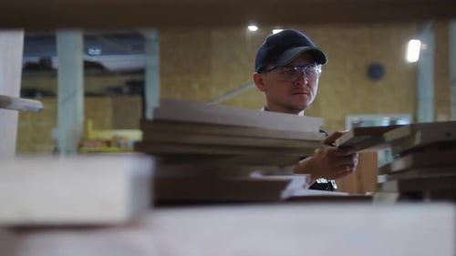 Carpentry Workshop a Man Worker Walks By the Shelves and Takes a Board Out of It