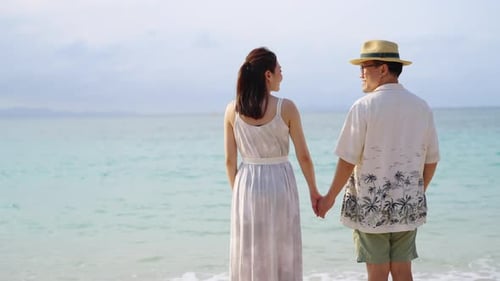4K Happy Asian couple holding hand and walking together on tropical beach at summer sunset