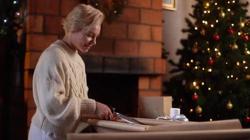 Woman Wrapping Christmas Gifts Near Fireplace and Tree