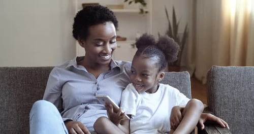 Mother and Daughter Use Smartphone Together on Couch