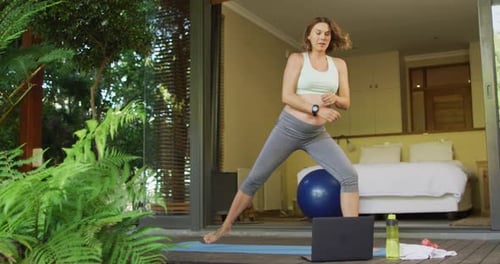 Woman Doing Yoga on Deck Near Tropical Plants