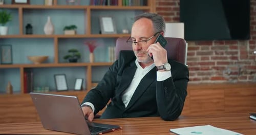Man Working on Laptop and Talking on Phone