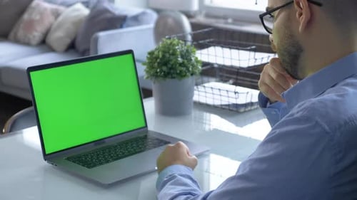 Over the shoulder shot of man working on laptop with green screen display