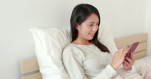Young Woman Relaxing in Bed Using Smartphone