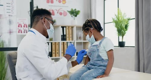 Doctor in Facial Mask Doing Injection in Small girl's Arm During Her Visit to Clinic