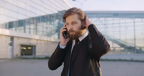 Empleado de oficina que habla por teléfono cerca de un moderno edificio urbano de vidrio