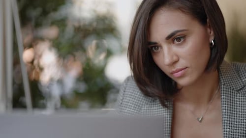 Hispanic Woman is Sitting on a Chair and Writing Down or Taking Down Notes While Attending an Online