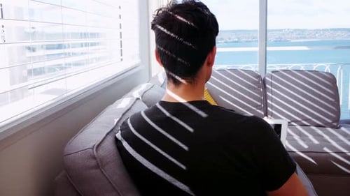 Man Relaxing on Couch Using Tablet Near Window