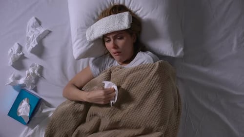 Femme malade avec compresse couchée dans son lit, toussant et éternuant, allergie saisonnière