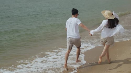 Young Asian couple in love holding hands and running on the beach cheerful happiness on holiday.