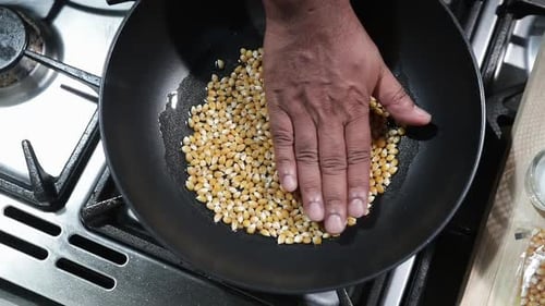 Hand Spreading Popcorn Kernels in Skillet