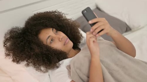Woman with Phone Lying in Bed