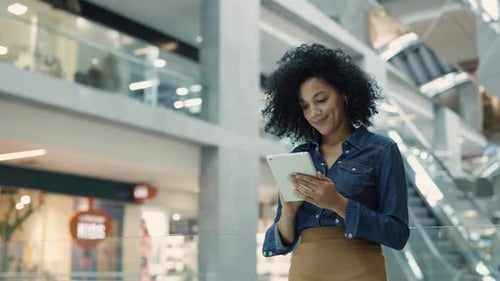 Woman Smiling Using Tablet in Shopping Mall