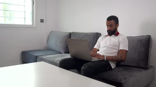 Man Works on Laptop on Couch at Home