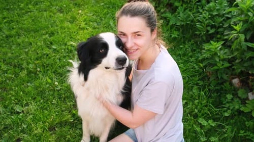 Lächelnde junge attraktive Frau streichelt und spielt mit süßem Hundewelpen Border Collie im Sommer im Freien