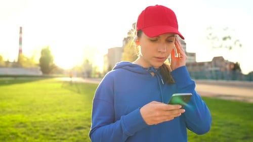 Woman with Wireless Headphones and Smartphone Chooses Music and Runs Through the Stadium at Sunset
