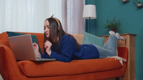 Young Woman Using Laptop Computer Sitting on Sofa at Home Working Online Shopping From Home Office