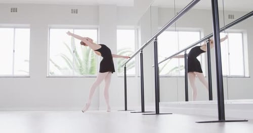 Caucasian female ballet dancer stretching up by the mirror in a bright studio