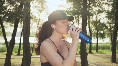 Woman Drinking Water in Sunlit Park After Workout