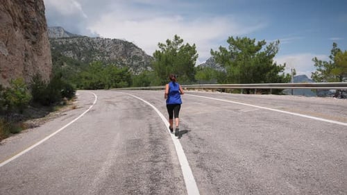 Woman running along rocky coastline with mountains on background