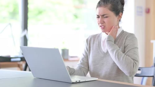 Young Woman Typing at Laptop Rubbing Neck in Pain