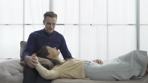 A happy western couple lying on sofa and talking to each other together
