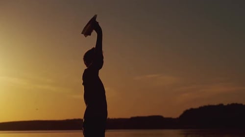 Silhouette of little boy sitting alone at the river on sunset background.