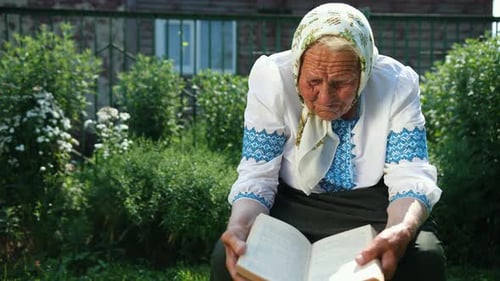 An Old Grandmother is Sitting on the Street and Reading a Book