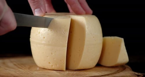 Male Hand Cut Off a Piece of Cheese on a Cutting Board.