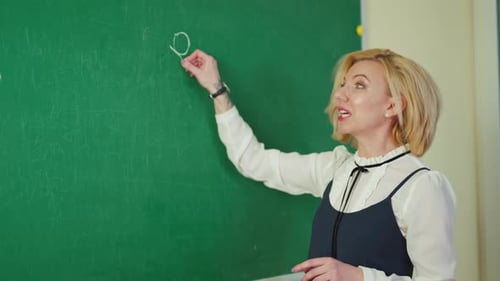 Teacher Writes on Chalkboard in Classroom