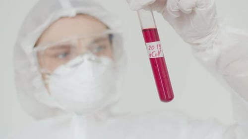 Una joven científica examina un tubo de ensayo rojo con una pegatina nCoV 2019. Una mujer en química