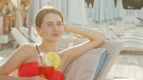 Lovely Young Woman Sipping Cocktail While Sunbathing at the Beach